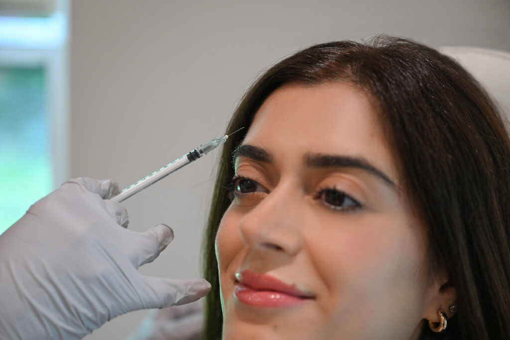 An injector is injecting a syringe of botox near Cleveland, OH, in a woman's forehead.