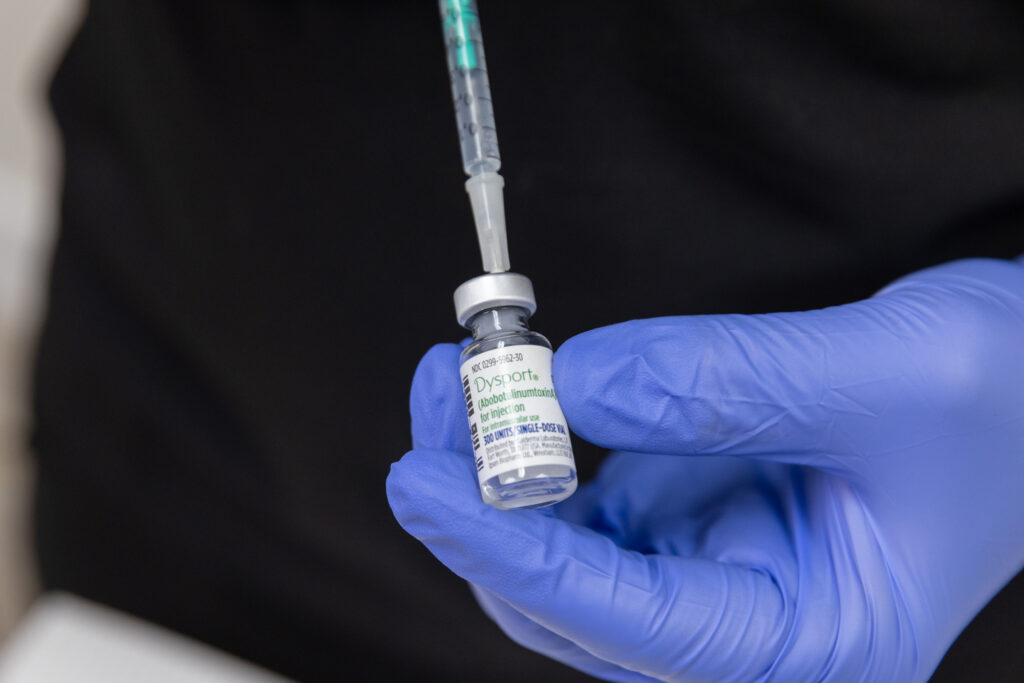 Close up of a gloved hand holding a vial of Dysport in Westlake, placing a syringe into it's cap.