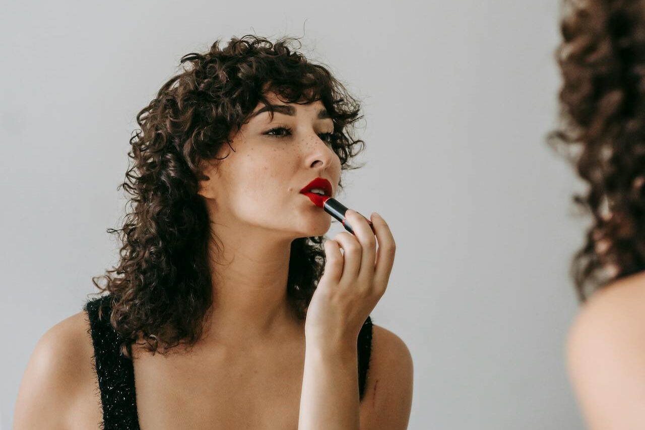 A woman purses her lips as she applies lipstick, a habit that can cause perioral lines. We can treat said lines with lip fillers in Westlake.